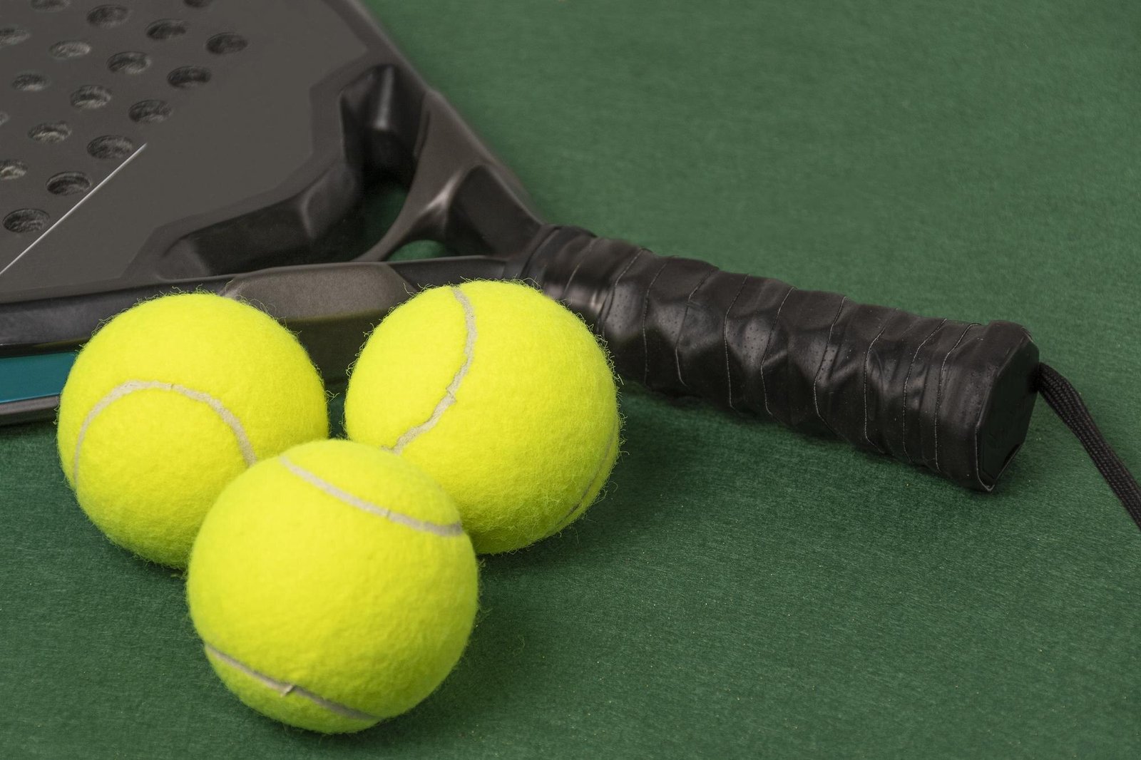 Pala de pádel y pelotas sobre una superficie verde
