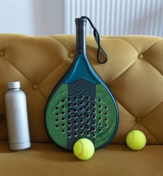 Pala de pádel, pelotas y botella de agua preparadas como equipo de juego