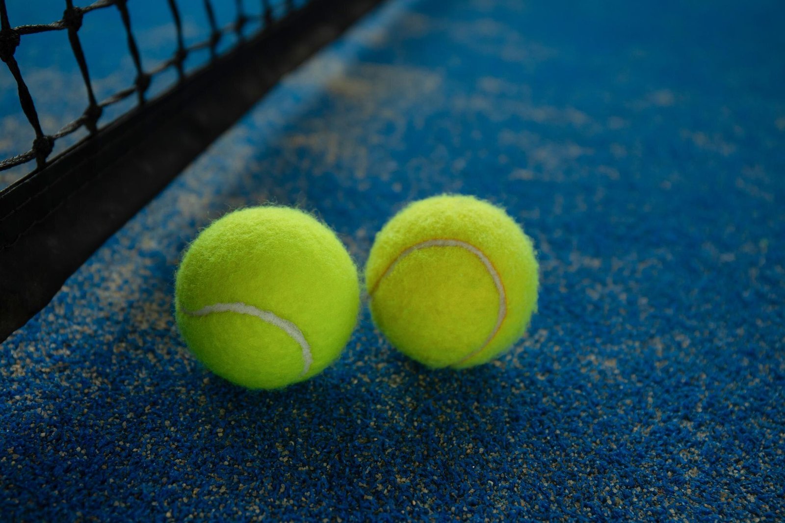 Pelotas de pádel junto a la red en una pista azul